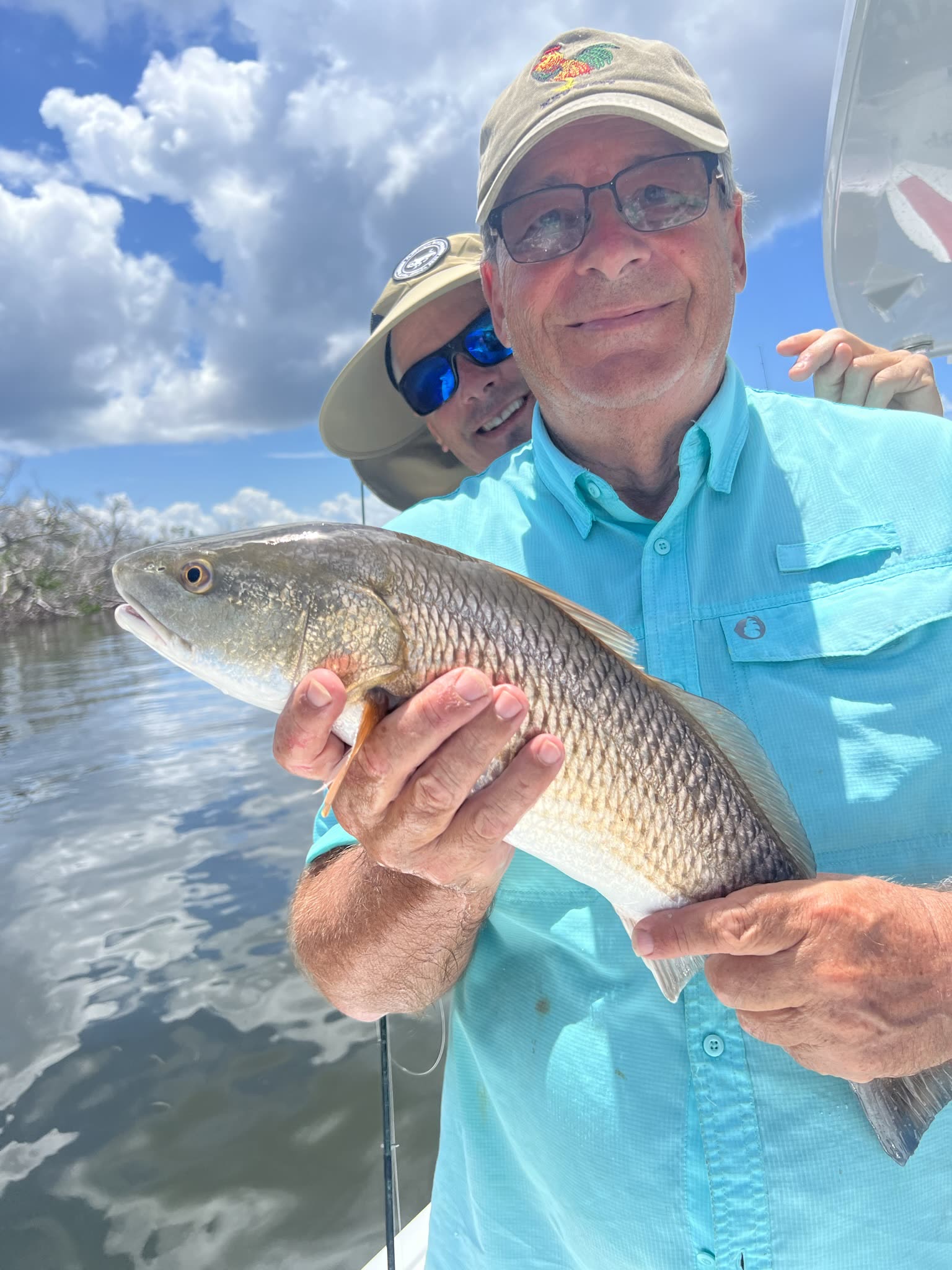 An angler holds a coppery-bronze redfish in a mangrove backwater