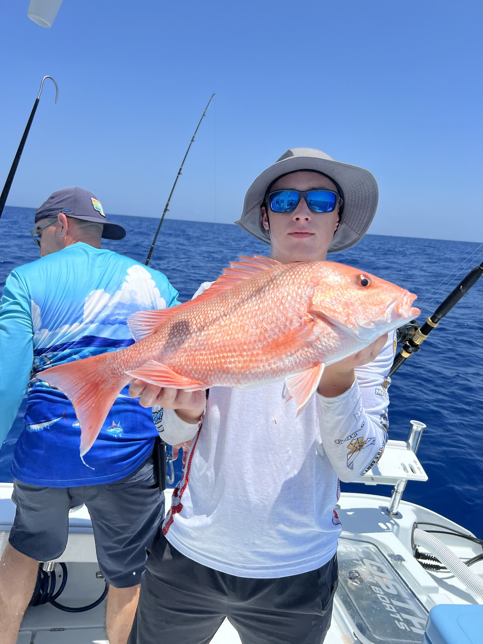 An angler holds a bright red snapper chest-high on a boat in open Gulf water
